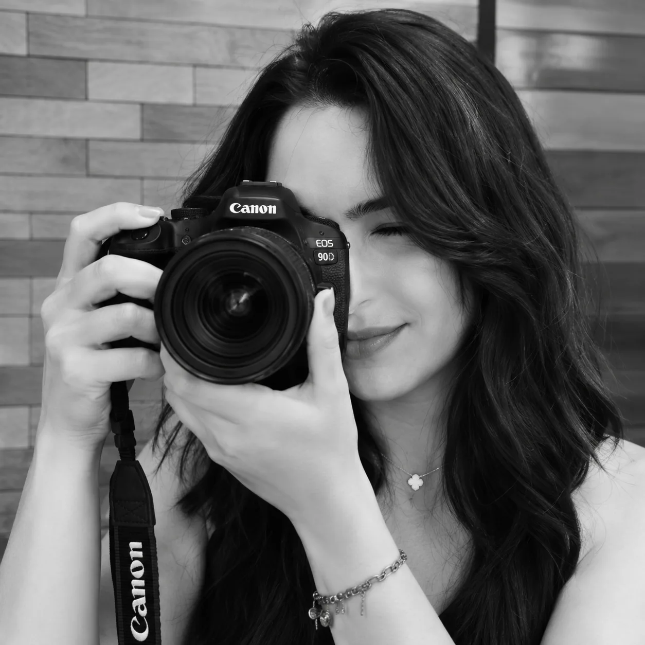 Nathalia Fagundes segura uma câmera junto ao rosto, em retrato preto e branco.