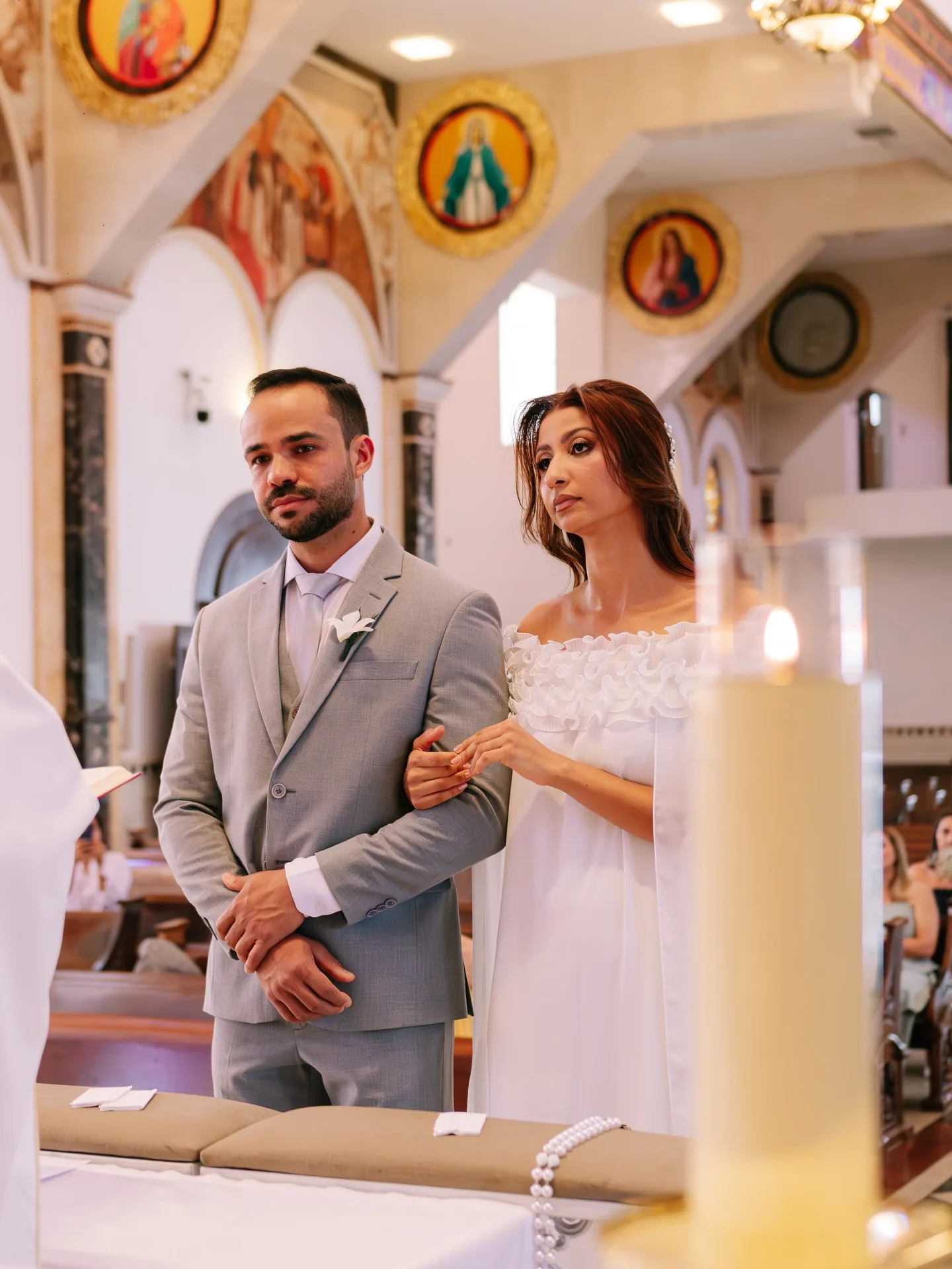 Casal de braços dados em uma igreja, ao lado de uma vela acesa.